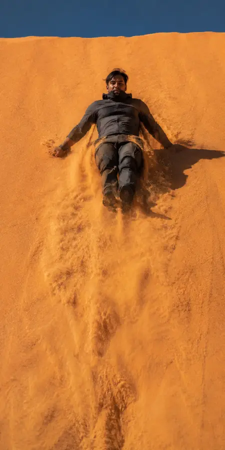 Man Sliding Down Steep Sand Dune — ue5 phone wallpaper